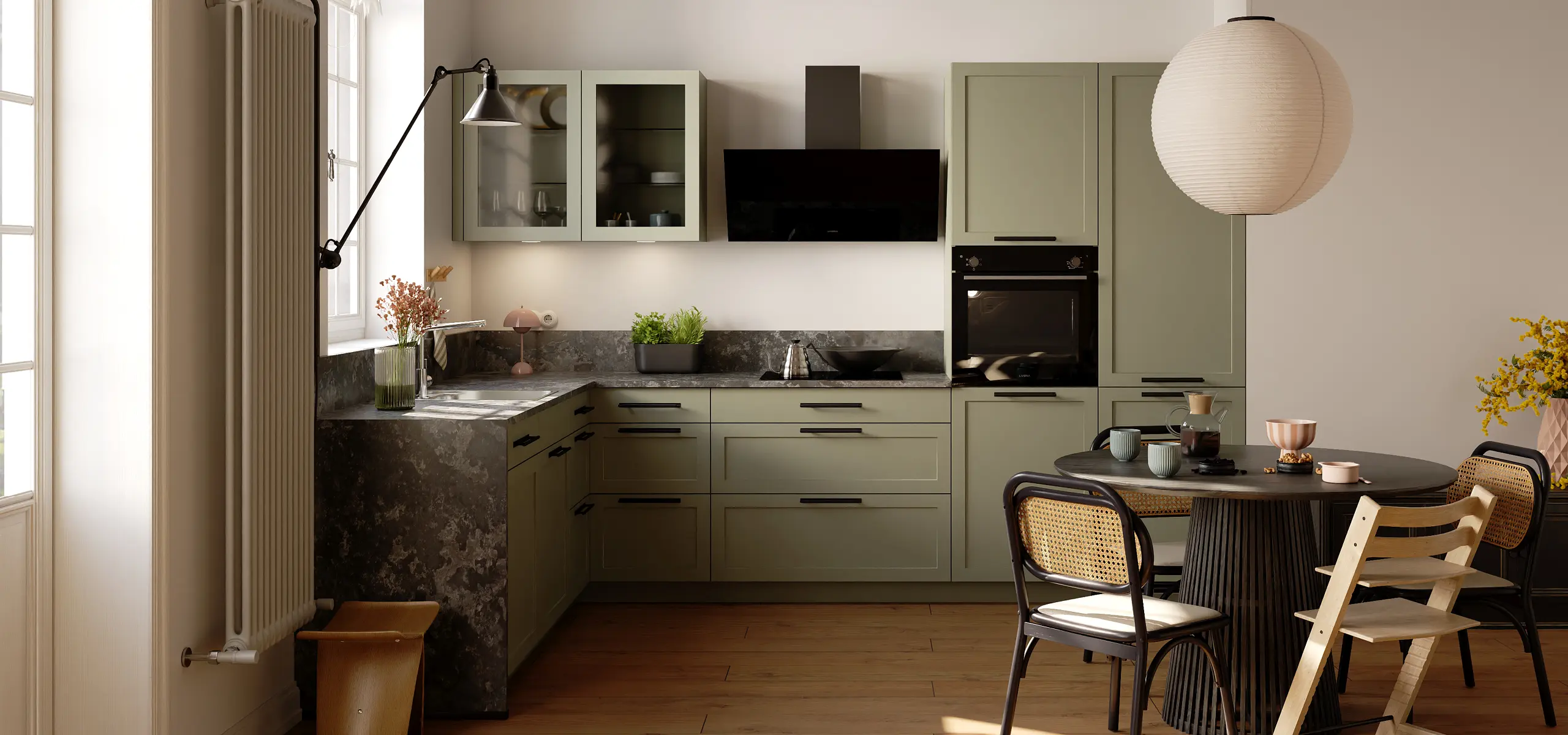 Klassische L‑Küche in Salbeigrün mit Rahmenfronten, dunkler Stein-Arbeitsplatte und großem Fenster; Doppelspüle mit Chromarmatur, Glas-Hängeschränke, schwarze Schräghaube, Induktionsfeld mit Kessel und Wok, Kräutertopf, Holzfußboden.